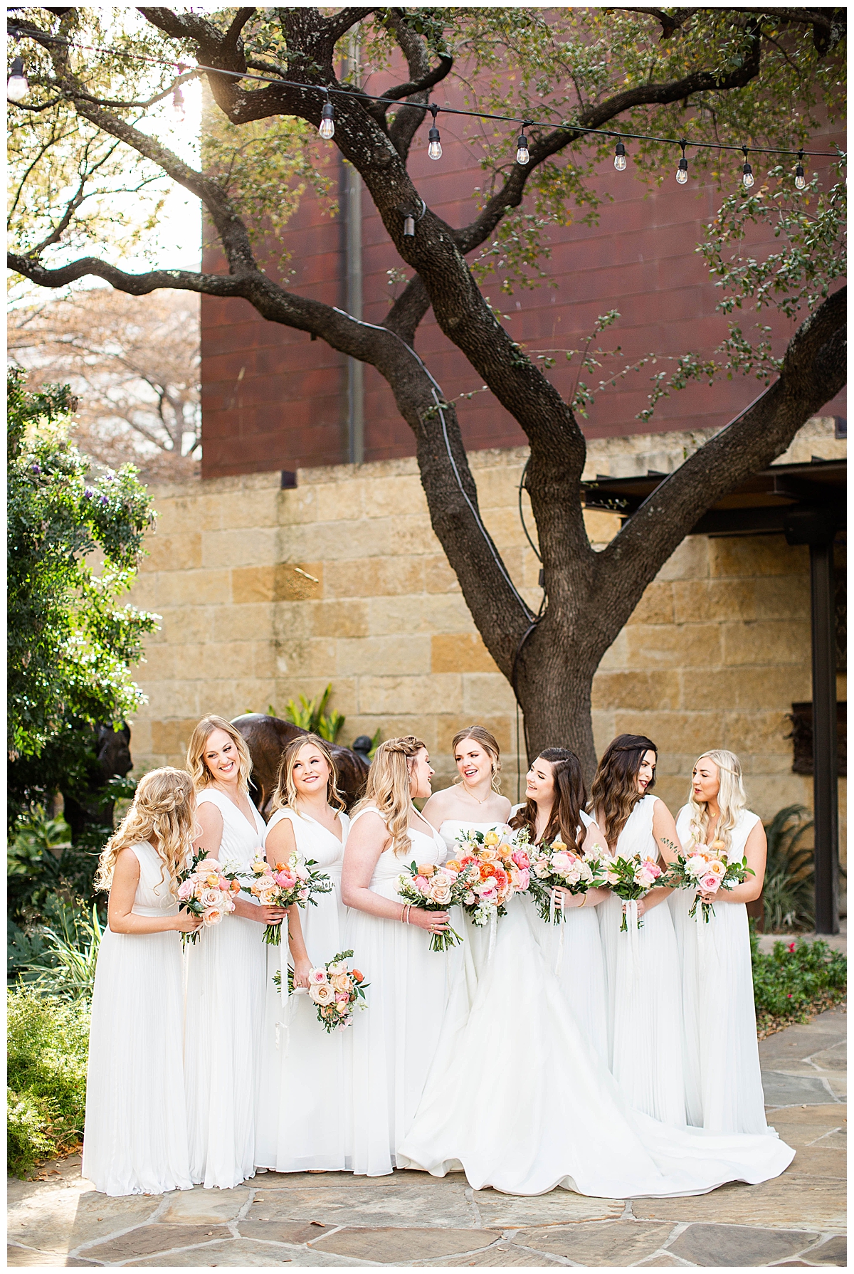 Bridesmaids in white dresses smile and laugh with their bouquets. 