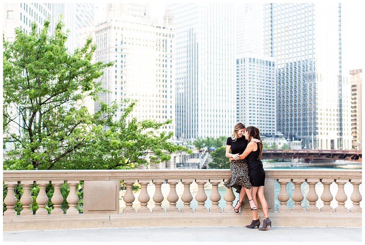 A couple embraces at the Wrigley Building in Chicago. They are taking their engagement portraits. They are wearing all black in a stylist way.