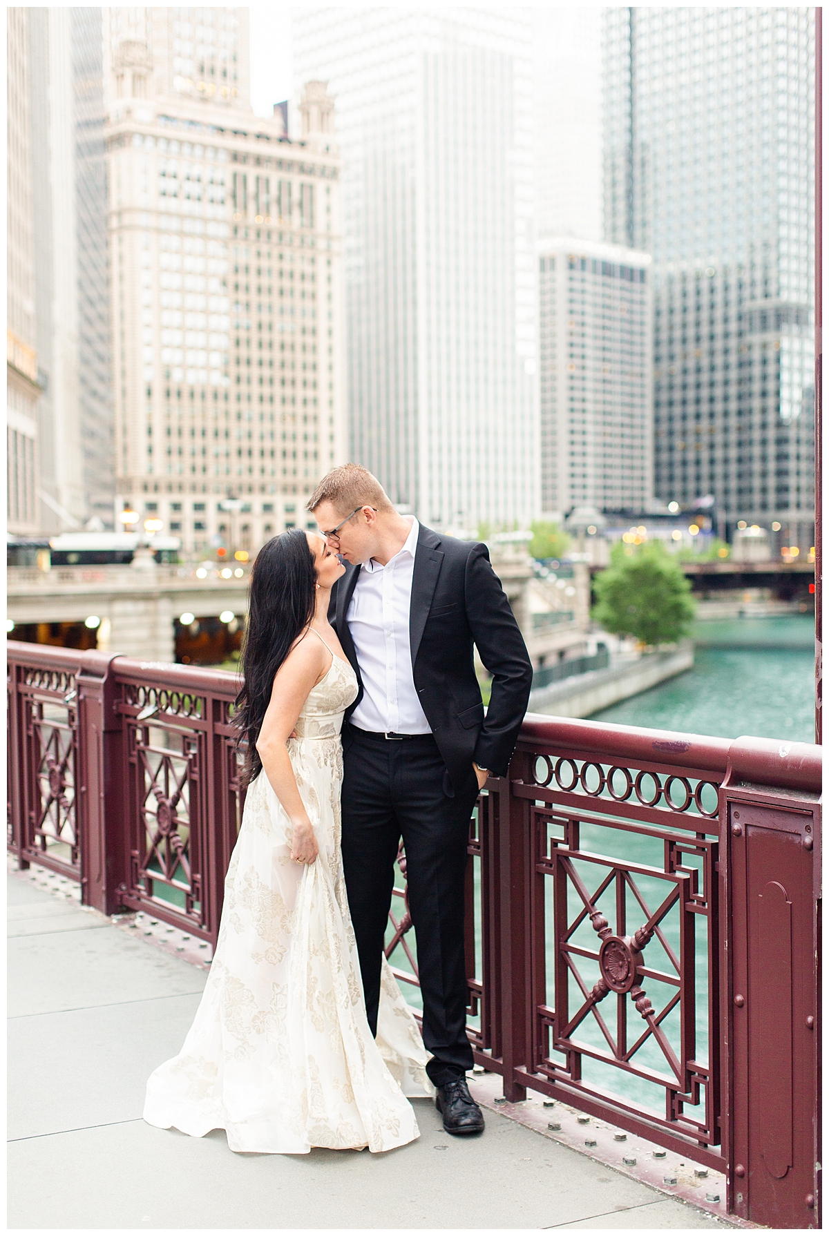 A couple kisses on a red bridge outside of the Wrigley building in Chicago. This is their engagement picture and they are dressed very formally. 