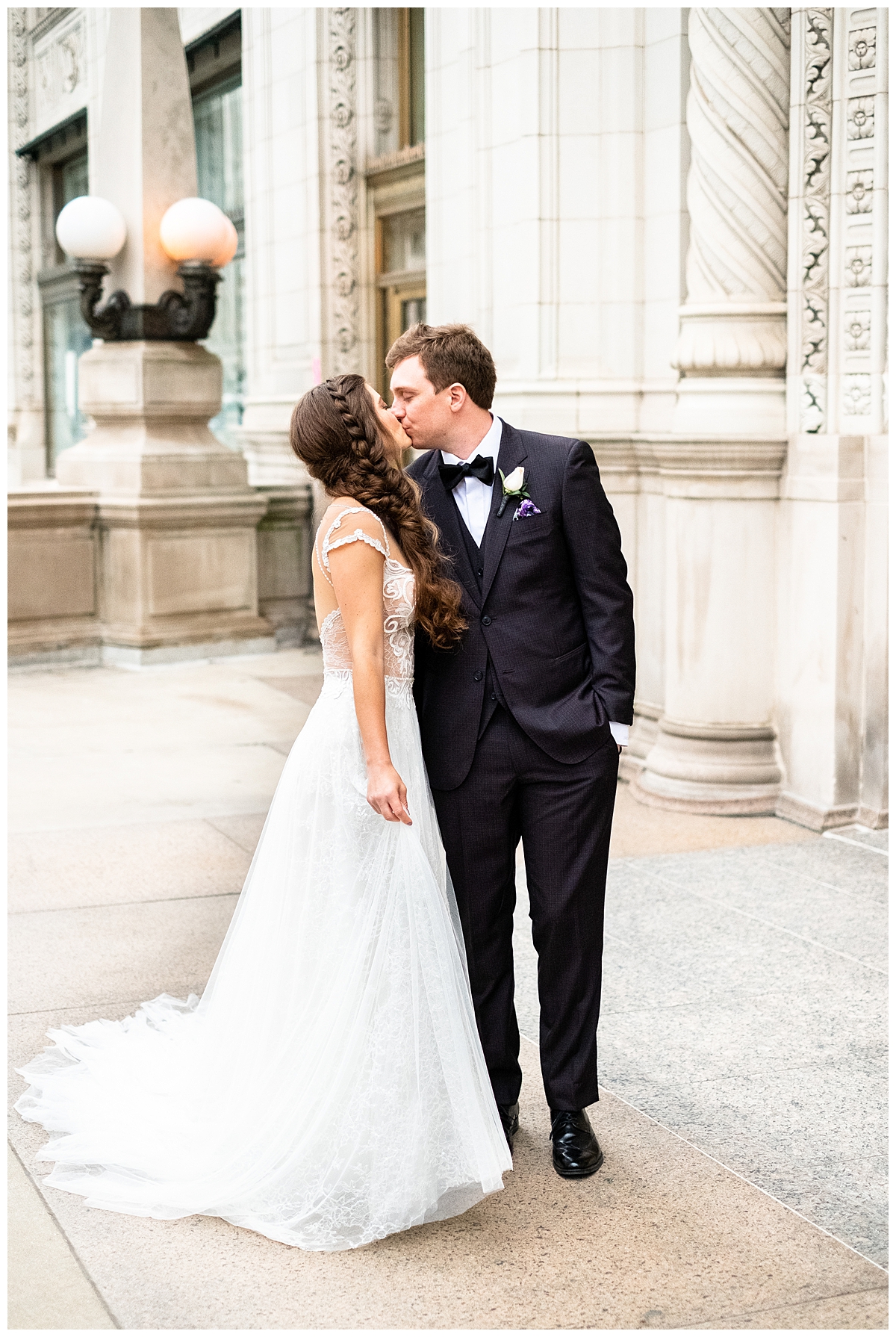 A bride and groom kiss in a wedding portrait outside of Wrigley Building in Chicago. They are dressed in formal wedding attire. 