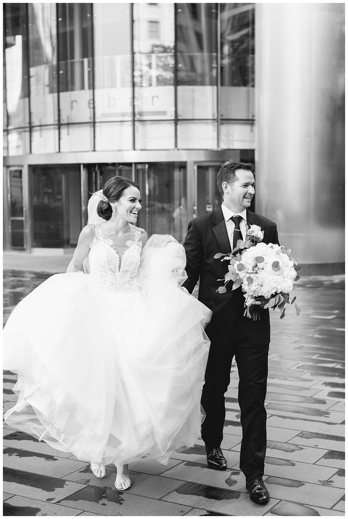 A bride and groom smiles in this black and white wedding portrait outside of the Wrigley Building in Chicago. They are dressed very formally. 