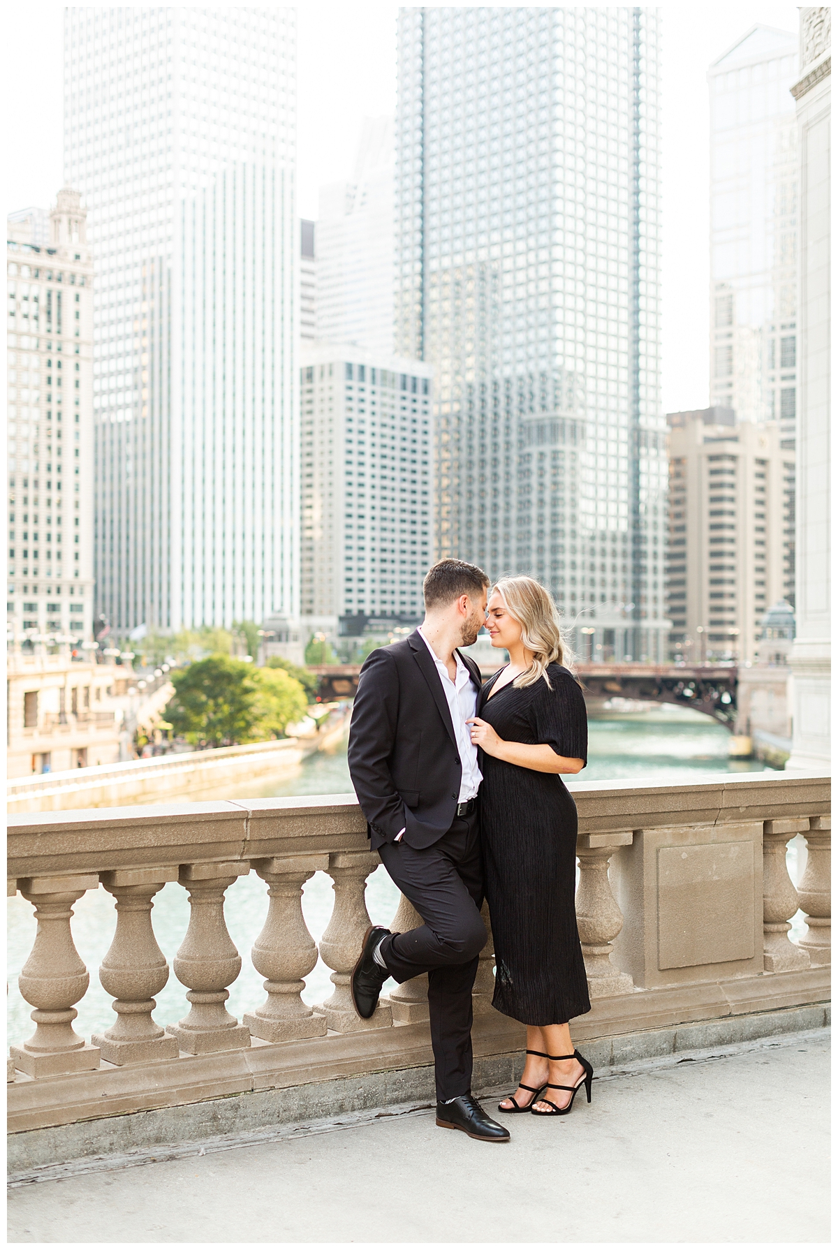 A couple takes their engagement portrait outside of the Wrigley Building in Chicago. They are stylishly dressed in all black. 