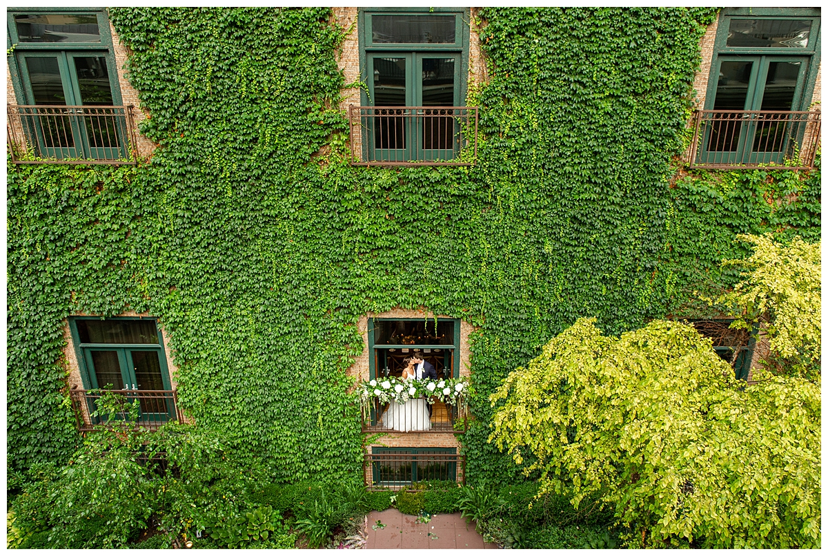 The bride and groom are photographed from the rooftop, peaking through a window in the courtyard into the ballroom at the Ivy Room in Chicago. 
