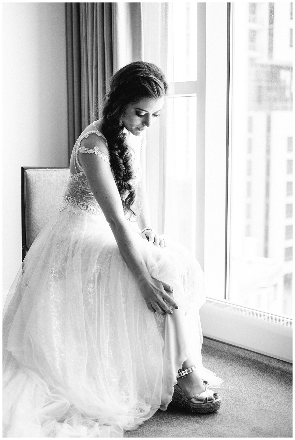 A bride in her wedding gown poses by a window. 