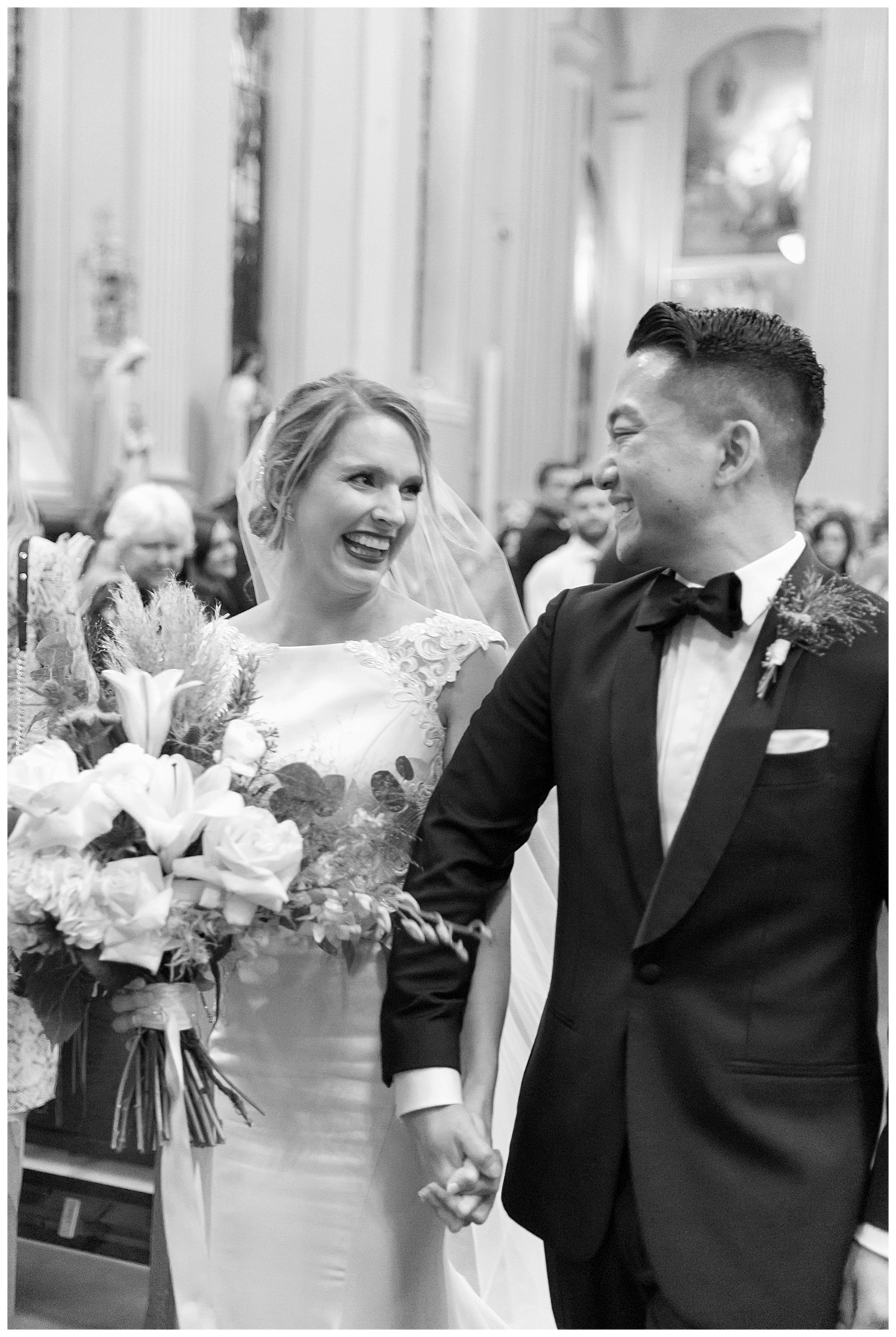A bride and groom smile in a black and white portrait exiting their ceremony. 