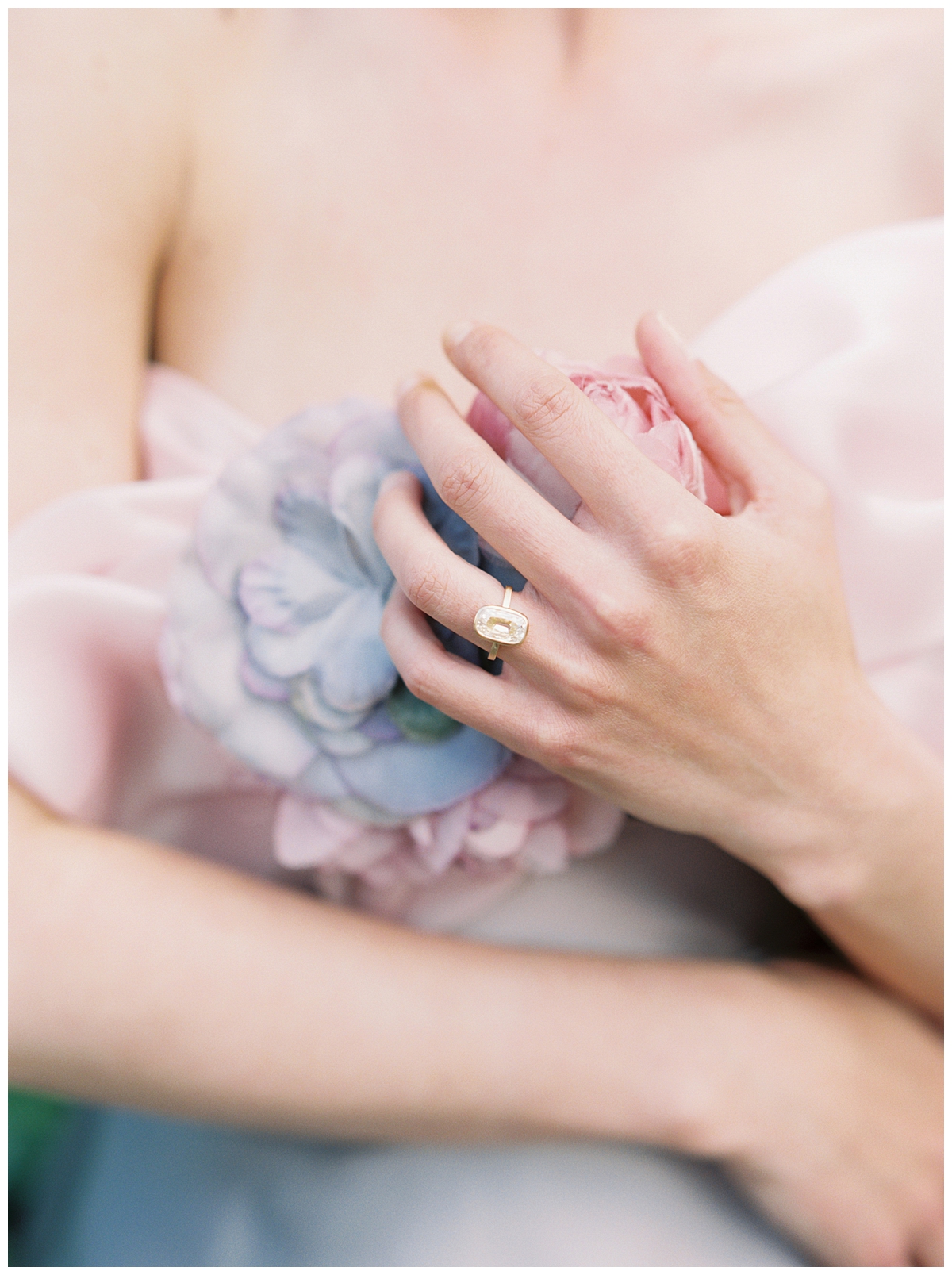 A bride holds a pink and purple hydrangea, displaying her engagement ring. 