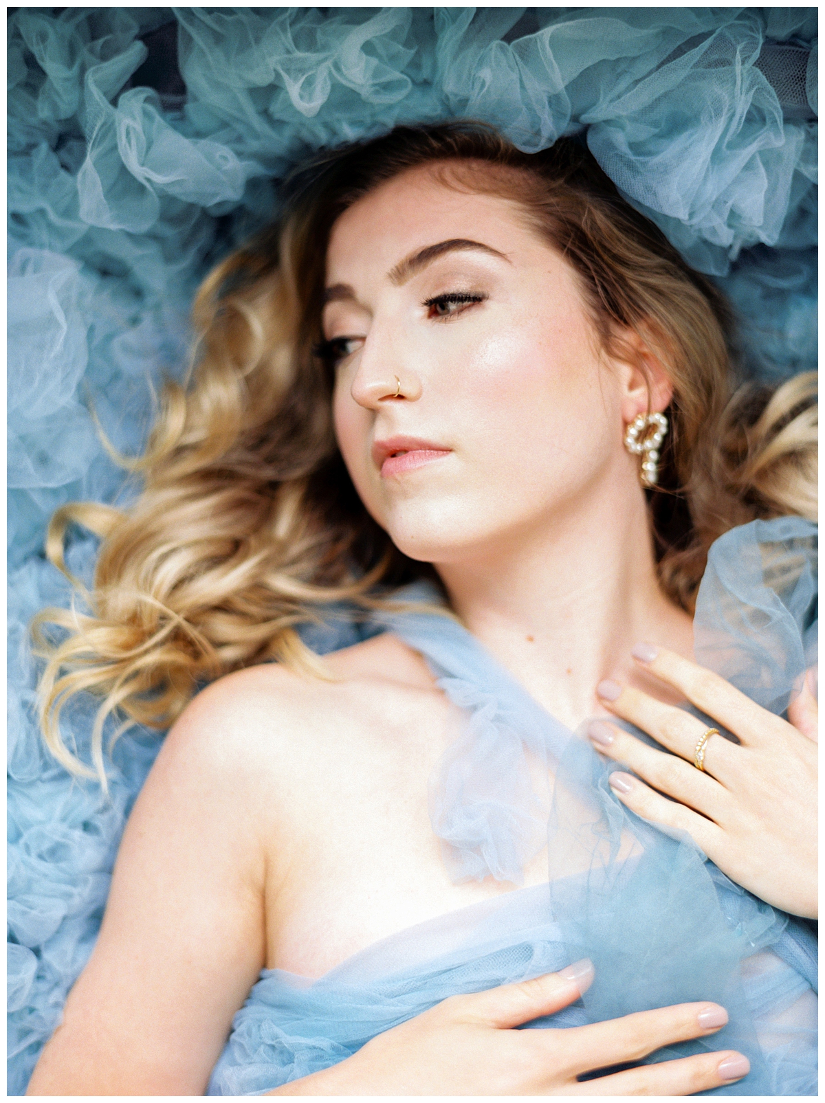 A woman poses laying on her periwinkle chiffon gown. 