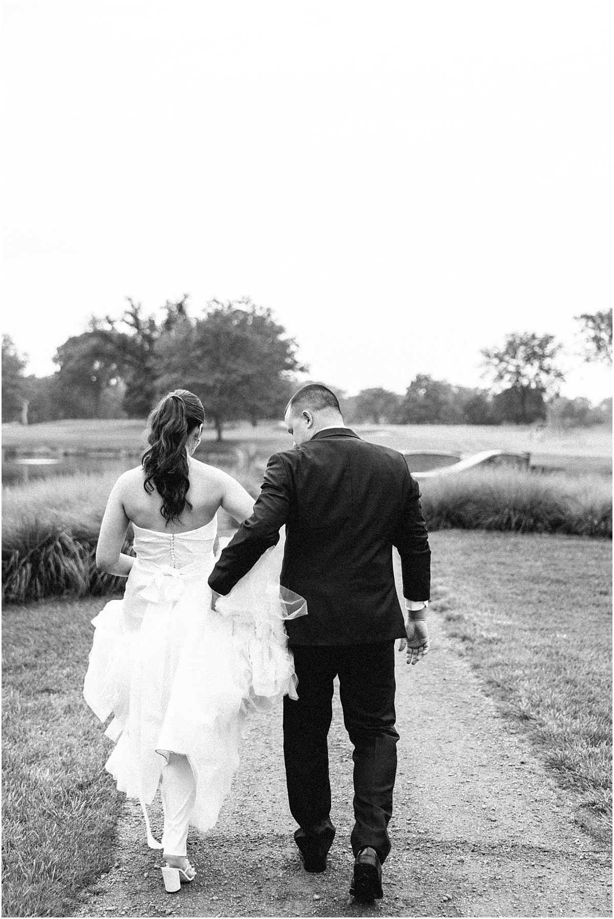 groom helps bride carry wedding dress as they walk