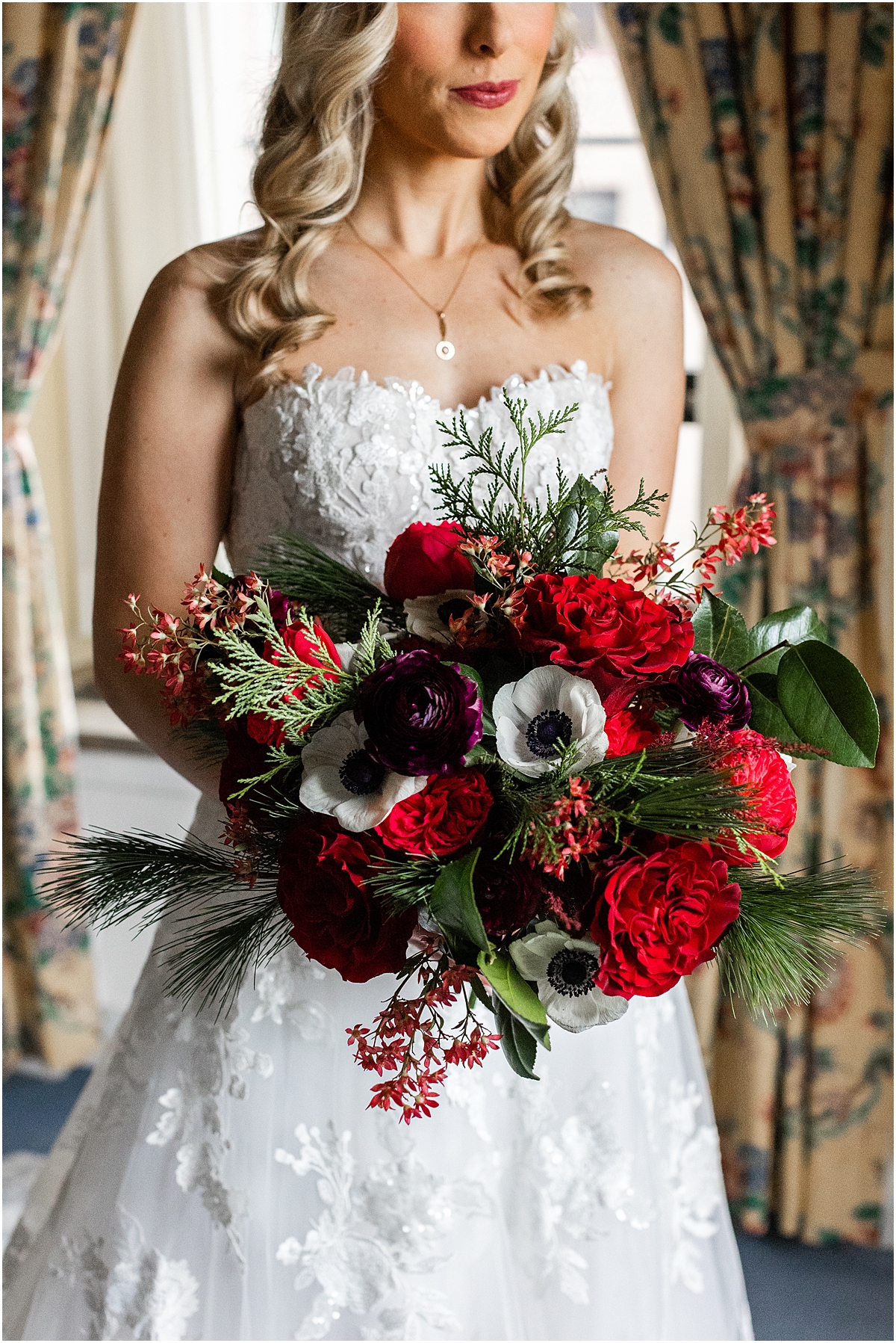 bride holding red and white bridal bouquet featuring evergreen sprigs
