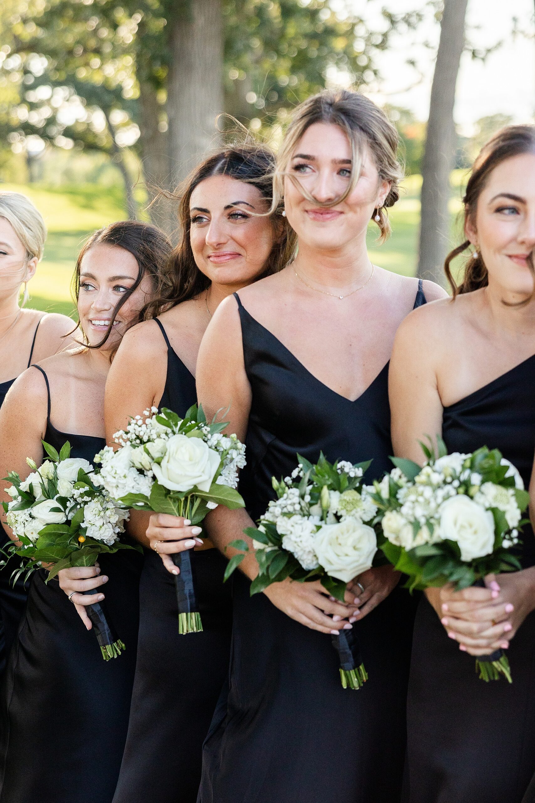 bridesmaids in black dresses holding white flower bouquets 