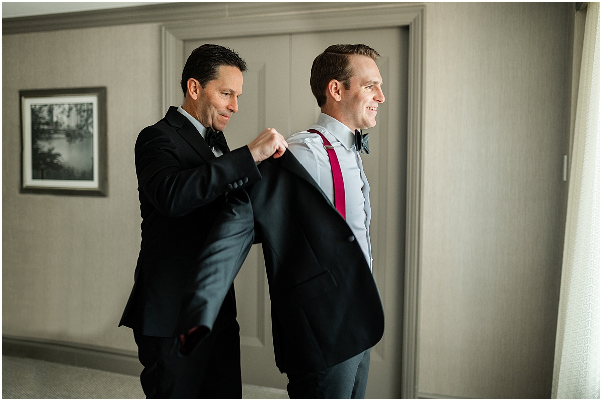 groom puts on suit jacket with help from best man
