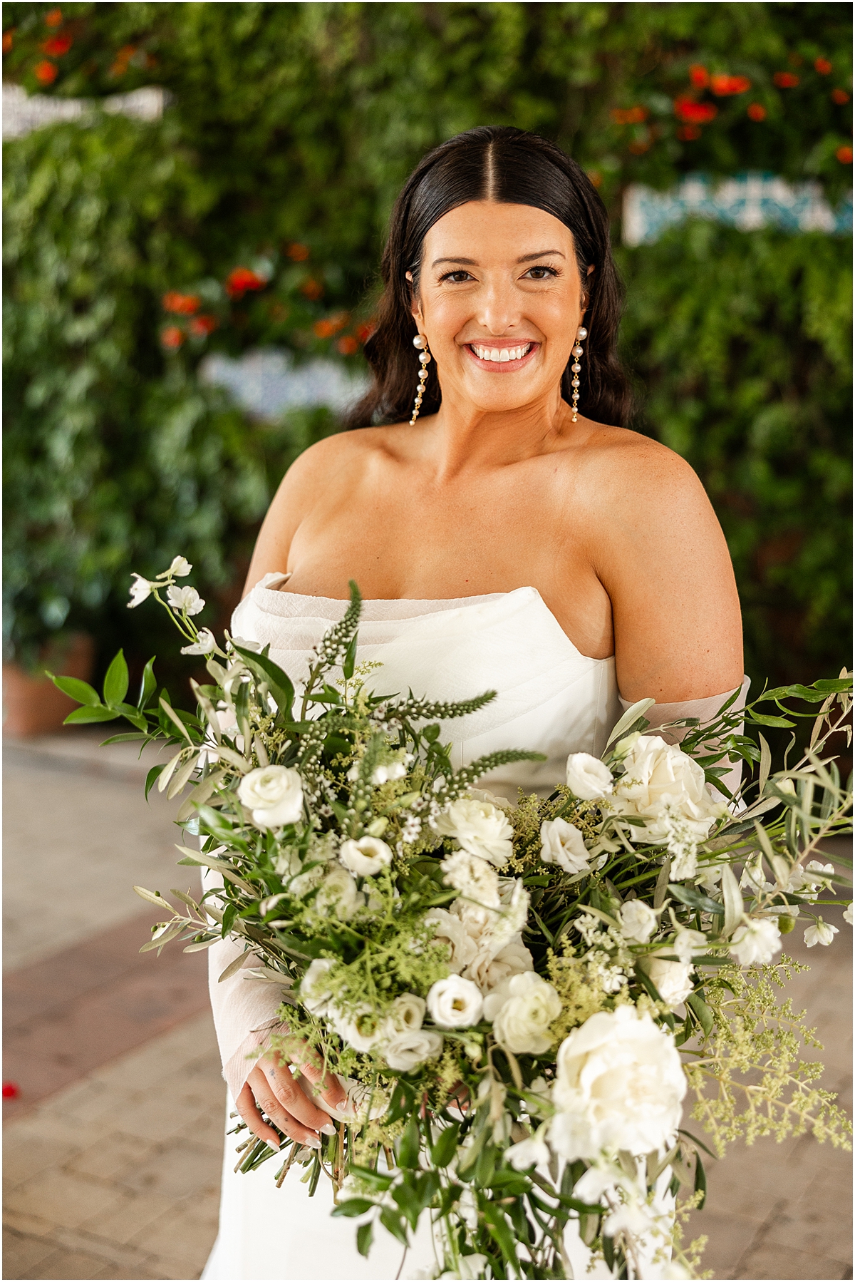 bride in strapless gown holds large bouquet of white flowers with sprigs of greenery