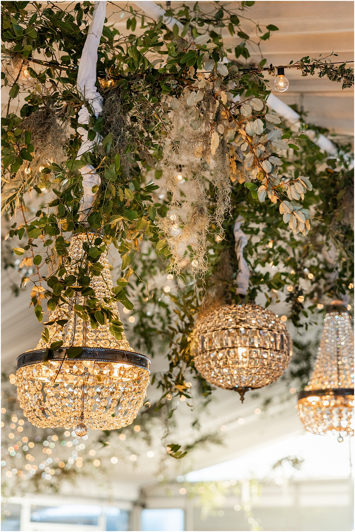 crystal chandeliers and greenery hanging from ceiling at wedding reception