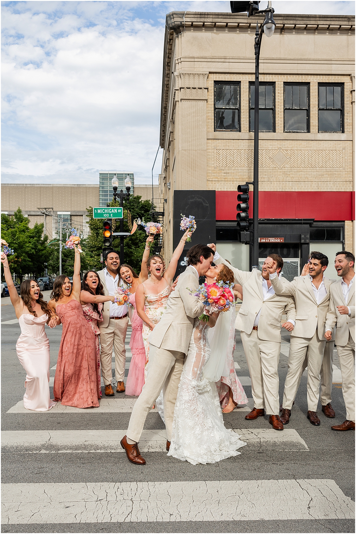 wedding party cheers as bride and groom kiss in the middle of street
