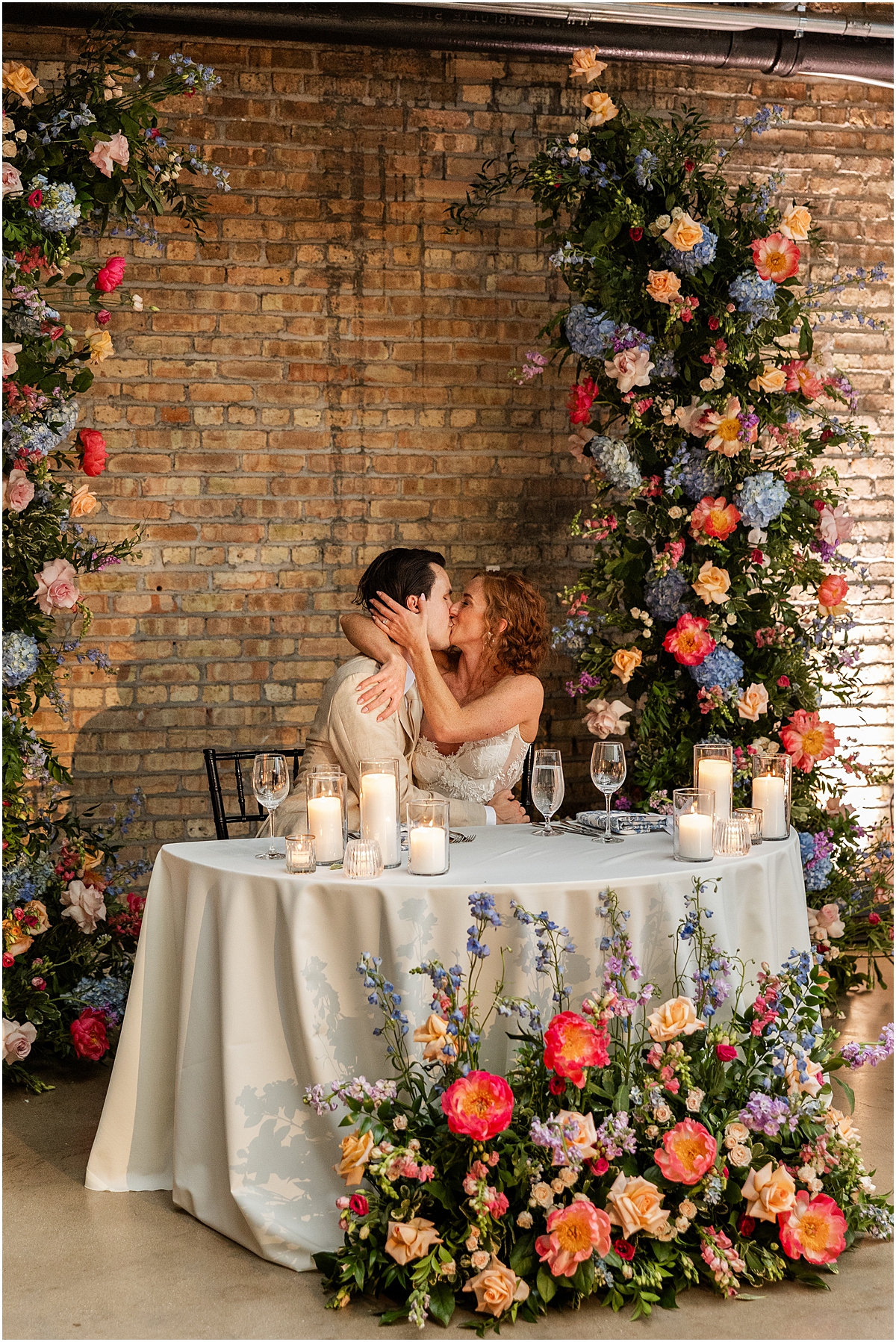 bride and groom kiss at head table surrounded by colorful florals