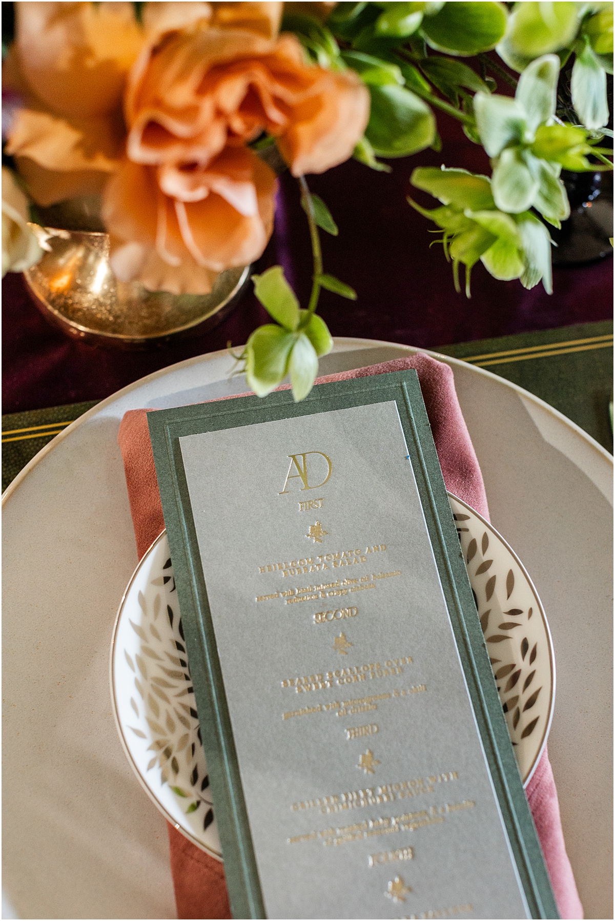layered place setting with pink napkin, patterned plate and dark green bordered menu