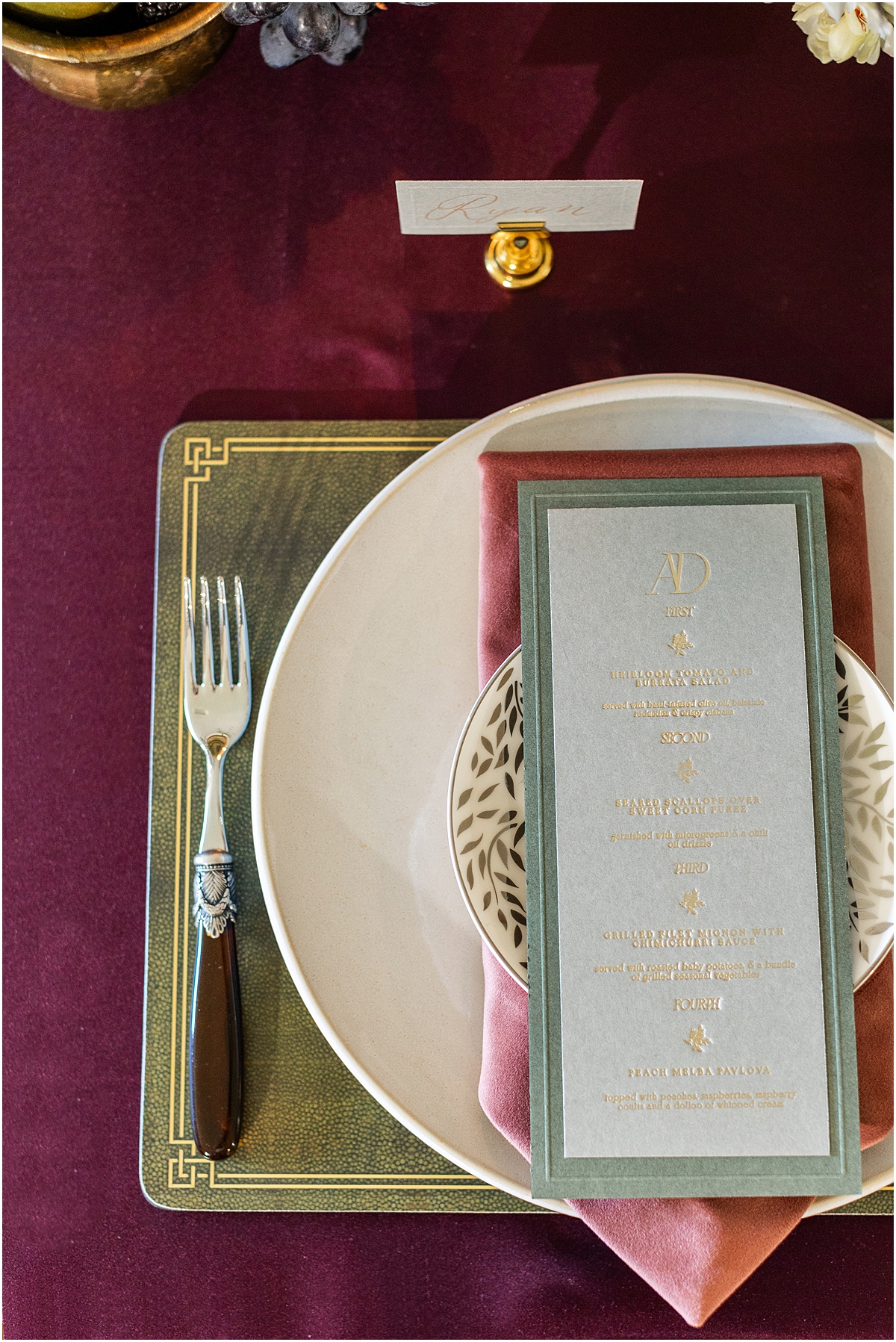 layered place setting with pink napkin, patterned plate and dark green bordered menu