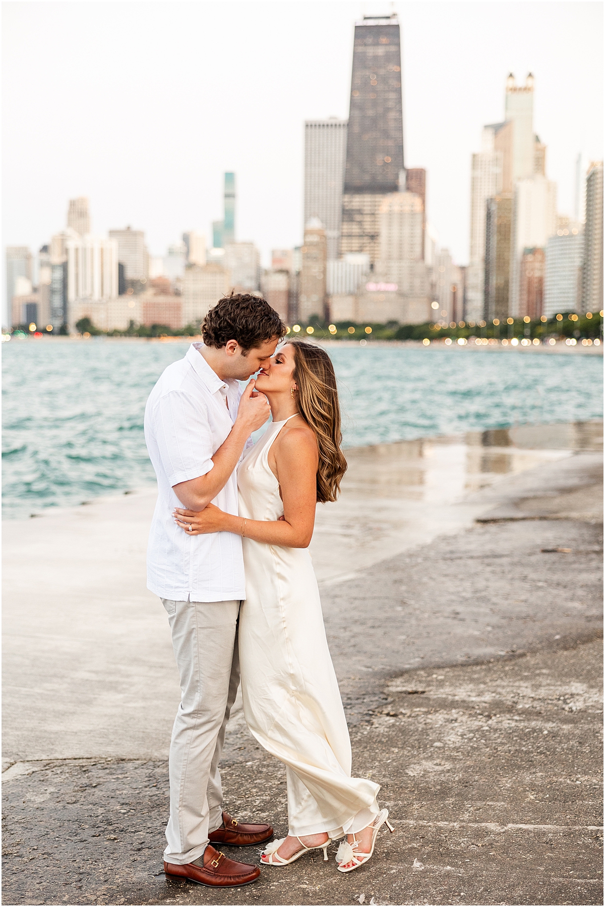engaged couple kiss by the water with Chicago skyline in the background 