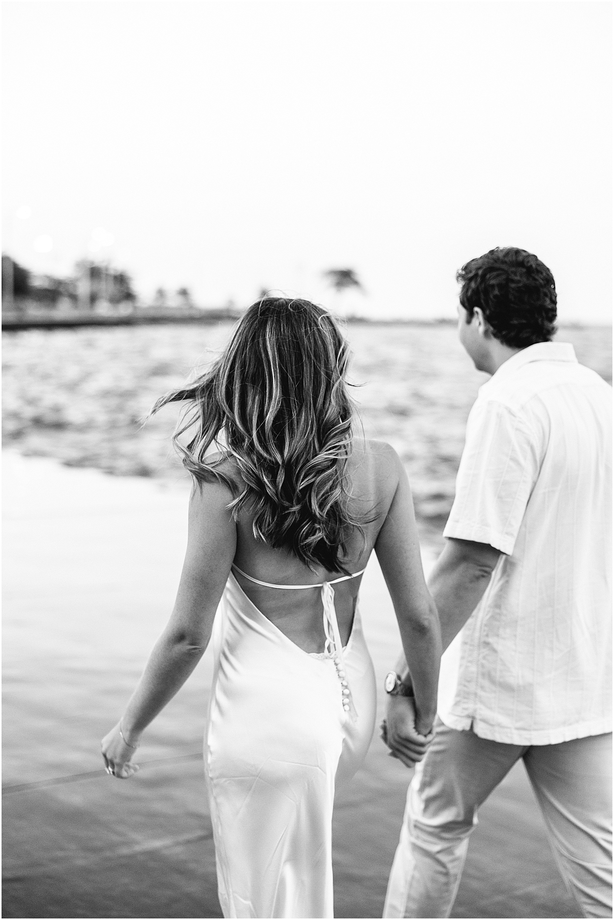 couple hold hands and walk along the water