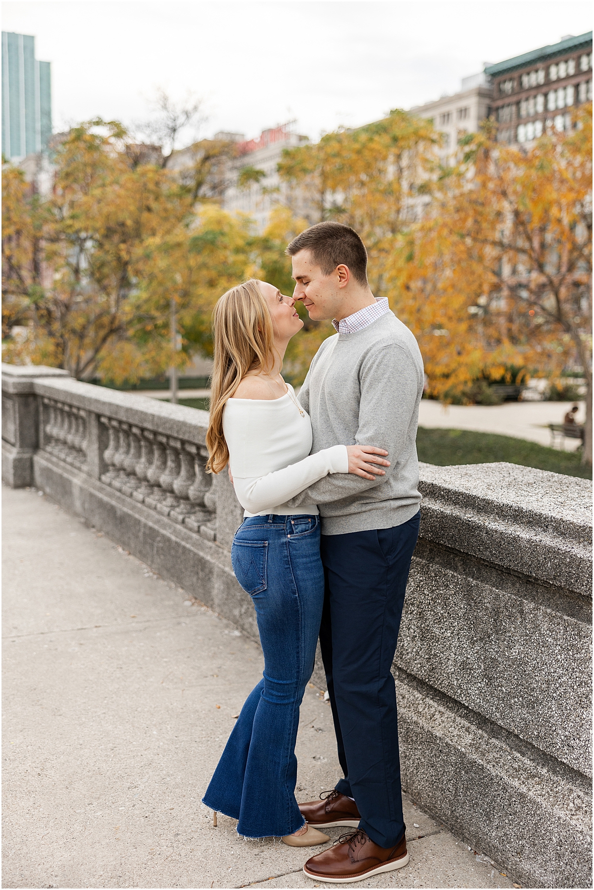 couple lean in together with fall trees in the background 