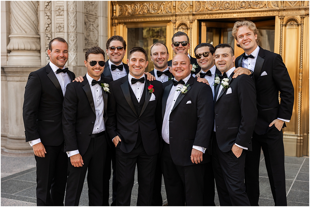 groomsmen surround groom outside of Wrigley building in Chicago 